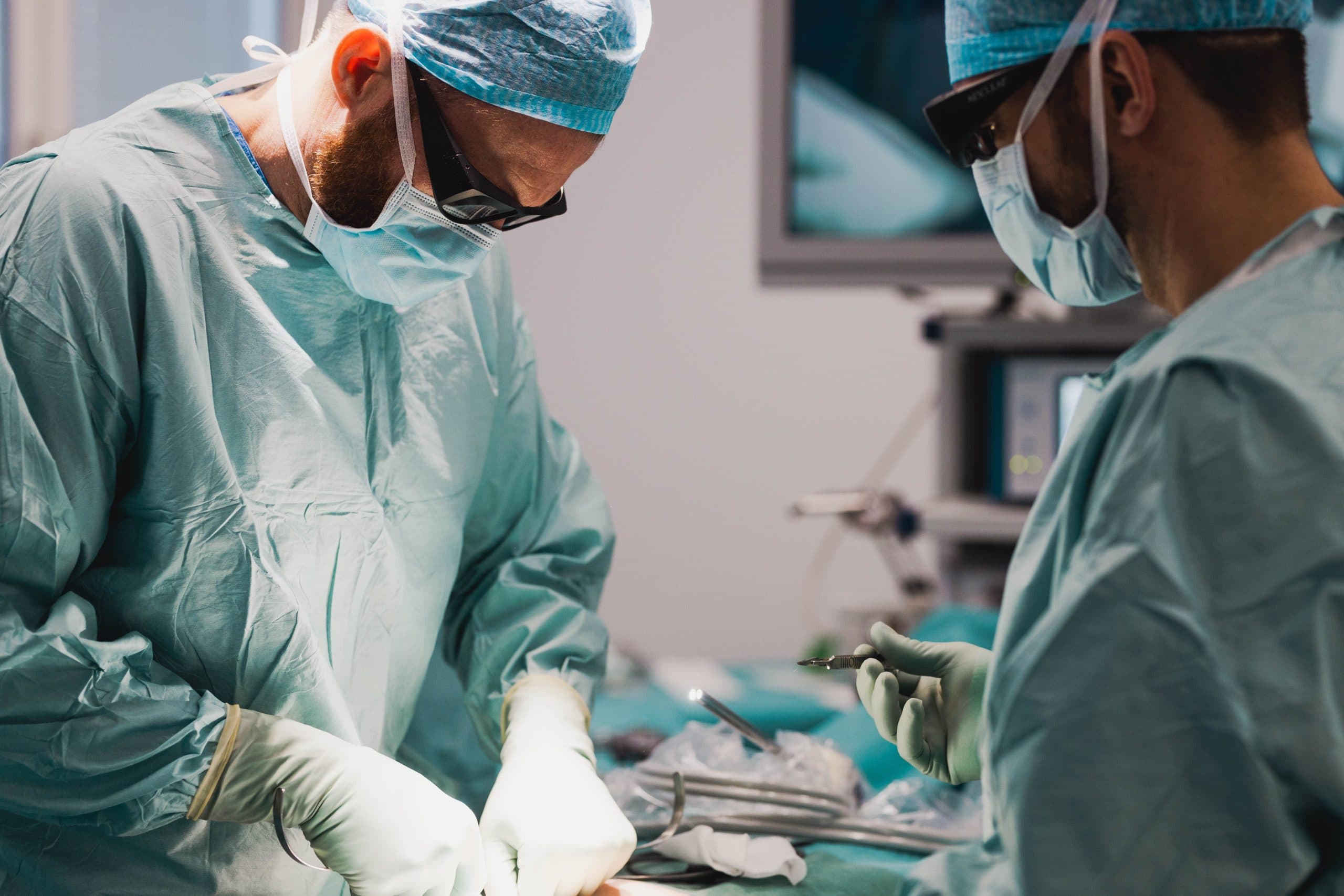 Två kirurger i operationssal, nära patienten och med fokus på operationen.